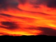 Red, orange, purple, and yellow swirl above the silhouette of a mountain range.