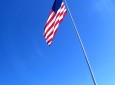 The US Flag flutters in the wind atop a long pole.